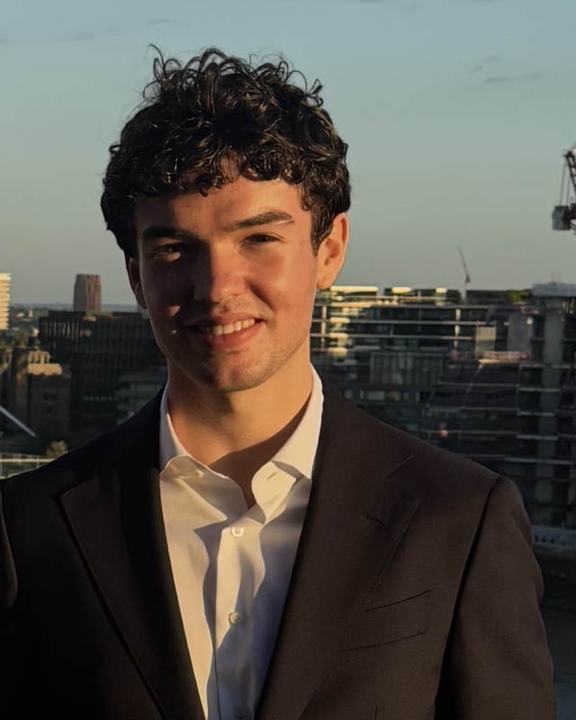 Conor Linkston in a dark suit on a rooftop terrace in London at sunset